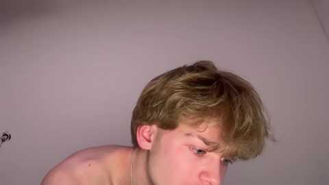 Video of a young, fair-skinned, short-haired boy with messy hair, looking down, wearing no shirt, against a plain, light gray background.
