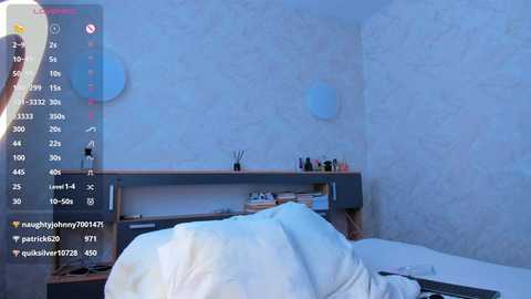Media: Video of a minimalist bedroom with light blue walls, a cluttered desk, and a messy bed. The scene includes a digital overlay showing social media metrics.