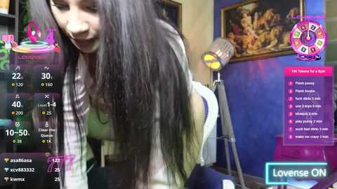 Video of a young woman with long black hair, wearing a plaid shirt, bending over a table, in a brightly lit room with blue walls and art. Live streaming overlay shows viewers' names and chat.