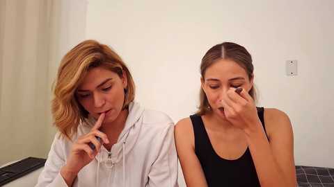 Media: Video of two women, one in white robe, the other in black tank top, both with blonde hair, sniffing a white substance.