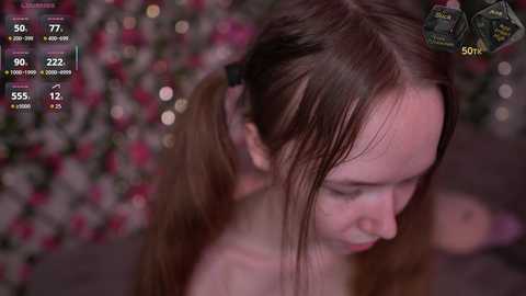 Video of a young woman with fair skin and long brown hair, partially tied back. She has a contemplative expression. Background features a blurred floral pattern. Video recording interface with time, date, and camera settings visible.