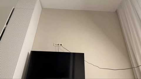 Video of a corner room with a beige wall, white vertical blinds, a black TV, and a coiled white cable.