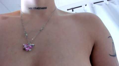 Video of a topless woman with light skin, wearing a necklace with a purple pendant, and \"MY CLIT IS A LITTLE SAD\" tattooed on her neck.