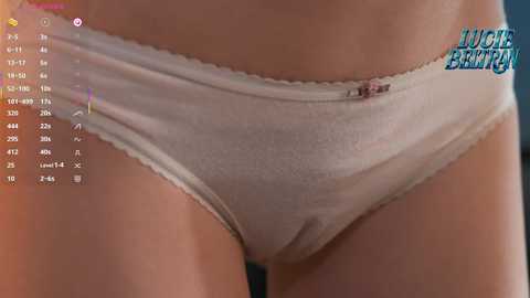 A close-up video of a woman's waist in white lace-trimmed panties, with a digital screen showing a fitness app interface in the background.