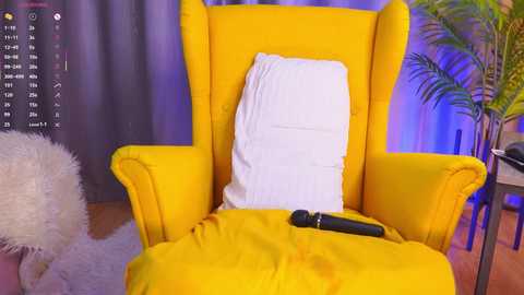 A video of a bright yellow, high-back armchair with a white pillow and black vibrator on a pink carpet, set against a purple and blue background with a potted plant.