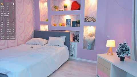 A video of a pastel-colored, modern bedroom with a light purple wall, white bedding, and built-in bookshelves with lit compartments.