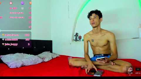 Video of a shirtless, slim, young Asian man with curly hair, wearing blue boxer shorts, sitting on a red bed in a brightly lit bedroom.