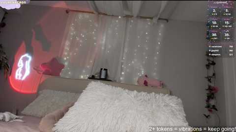 Video of a cozy bedroom with white bedding, a fluffy pillow, and a glowing neon sign. The background features a white curtain with fairy lights and a pink teddy bear.