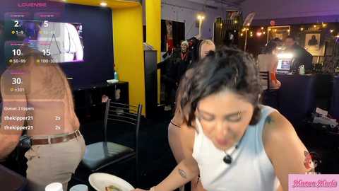 Media: Video of a lively bar scene with a woman in a white top and black pants, leaning forward to pour a drink. Background shows a TV displaying a basketball game, and a man in a dark shirt.