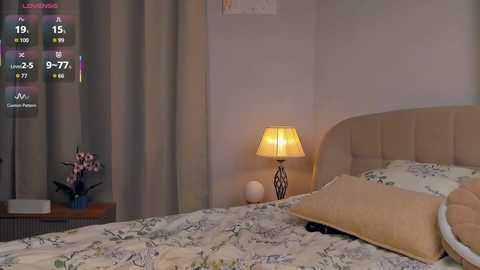 Video of a cozy bedroom with a beige headboard, floral bedspread, white pillows, and a small table lamp.