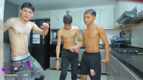 Video of three shirtless young Asian men in a modern kitchen, one leaning against a black fridge, the others in black pants, smiling.