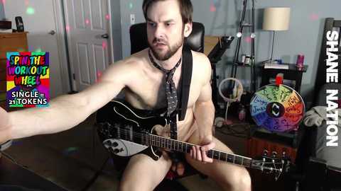 Media: Video of a muscular, bearded man playing an electric guitar, shirtless, with a colorful, psychedelic poster in the background.