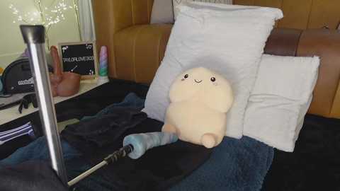 Media: Video of a plush white bunny on a bed with a brown headboard, surrounded by white pillows, a black blanket, and a pair of headphones on the floor.
