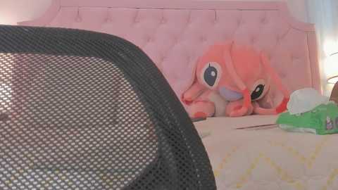Media: A video of a cozy, pastel-themed bedroom with a pink, tufted headboard and a soft, plush toy rabbit. The room features a green box and a black mesh chair in the foreground.