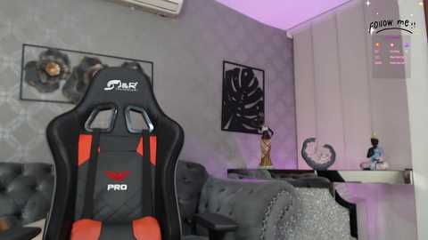 Video of a modern gaming room with a black and red \"SAR\" gaming chair, gray couch, gray walls, black framed art, and purple LED lighting.