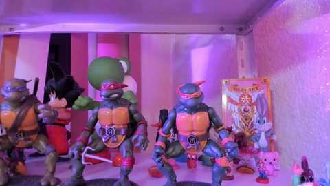 Video of a colorful, detailed toy display featuring Teenage Mutant Ninja Turtles figurines in various poses, against a pink, textured wall background.