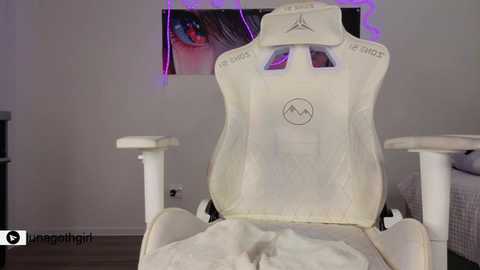 Video of a white gaming chair with a plush white blanket draped over it, set against a purple-lit room with a large eye mural on the wall.