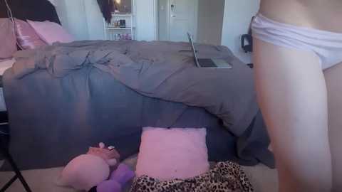 Media: Video of a messy bedroom with a woman in white panties, laptop open on bed, stuffed animals, pink blanket, and leopard print pillow.