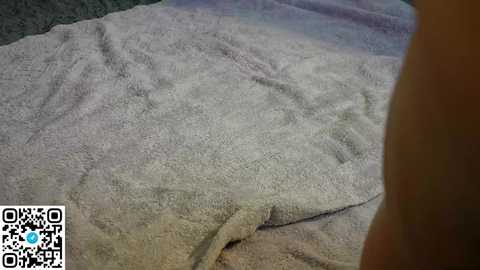 Video of a large, light gray, textured bath towel folded and laid on a dark gray, plush carpet. A QR code is in the lower left corner.