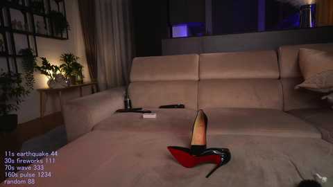 Video of a modern living room at night, featuring a beige sectional sofa with a pair of black high-heeled shoes and a glass of wine on a side table.