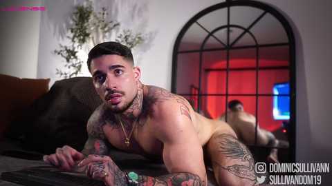 Media: Video of a muscular, tattooed man with short dark hair, lying nude on a bed, gazing into a mirror, surrounded by red and white lighting.