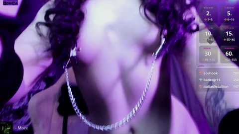 Video of a woman with curly dark hair, wearing a silver chain necklace, performing on stage. Background shows purple lighting, audience, and social media icons.