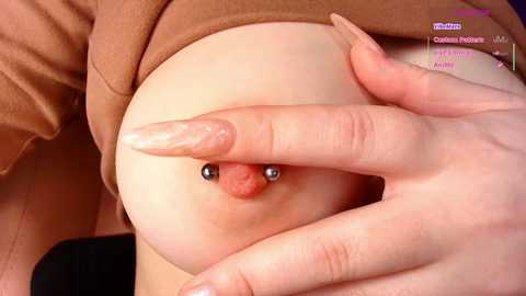 Video of a light-skinned person with a pierced nipple, using their long, manicured nails to pull at the areola.