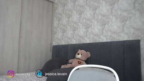 Video of a gray, cushioned headboard with a plush brown teddy bear resting on it, set against a textured, light gray wall.