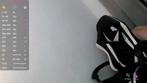 A video shows a hand holding a pair of black and white athletic shoes, set against a plain white background. A digital interface with a list of numbers and icons is visible on the left.