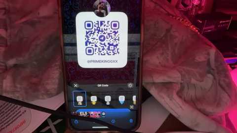 Media: A video shows a person holding a smartphone with a \"Prime Now\" app, displaying a QR code and product details. The background features a skull and crossbones fabric, partially draped over a wooden surface.