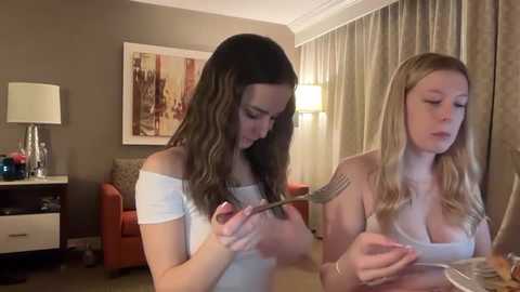Video of two young women with long hair, one braiding the other's hair in a cozy, beige-toned room.