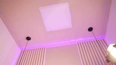 Video of a modern, beige-tiled ceiling with a white rectangular light fixture. Two black cylindrical wall sconces with black shades flank the light, and a striped beige and white rug is visible in the lower right corner.