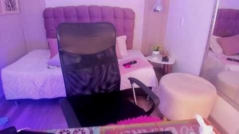 Video of a small, cozy bedroom with two twin beds, one with a white duvet and pink pillows, and the other with a gray duvet. A black office chair is in front, and a beige pouf is beside the mirror.