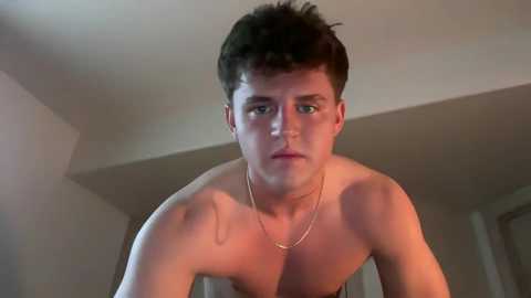 Video of a shirtless young man with short dark hair, fair skin, and a thin build, wearing a gold necklace, standing indoors against a plain, light-colored background.