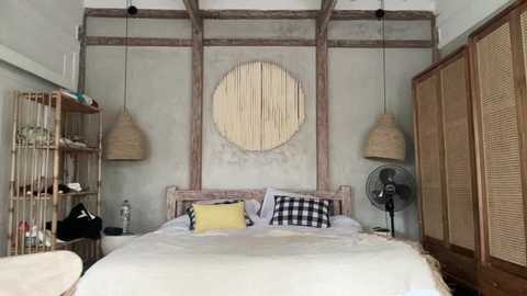 Media: A rustic bedroom with a wooden headboard, white bedding, a yellow pillow, bamboo pendant lights, and woven blinds, featuring a round, woven wall hanging.