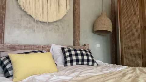 Media: Video of a rustic bedroom with a wooden headboard, beige and black checkered pillows, yellow throw pillow, macram\u00e9 wall hanging, wicker pendant lamp, and a beige wicker screen.