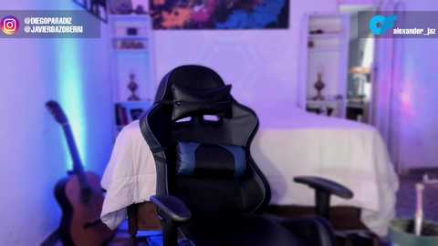 A video of a gamer seated in a black gaming chair with a white shirt, in a dimly lit, purple-hued bedroom with a guitar, bed, and wall art.