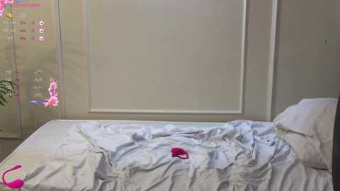 Video of a messy, unmade bed with white sheets and a pink vibrator on the pillow. The background shows a wall with a digital clock and a flower decal. The room is dimly lit.