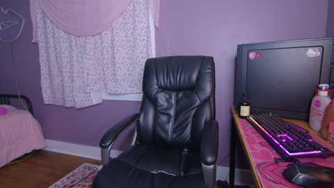 Video of a cozy gaming room with a black leather chair, pink curtains, a computer desk, and gaming keyboard.