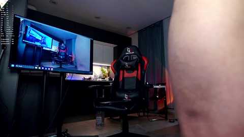 Video of a modern gaming room with a black and red gaming chair, large monitor, dark wood desk, and computer setup.