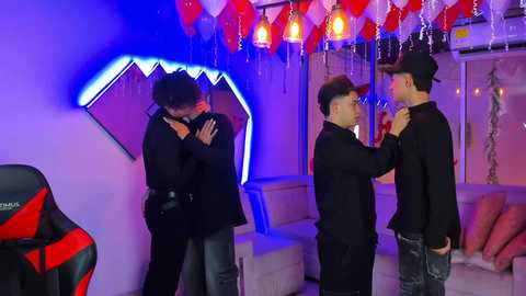 Video of two Asian men hugging in a dimly lit, modern room with neon shark teeth on the wall, red and white balloons, and gaming chair.