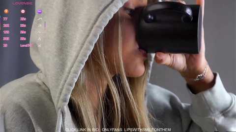 Video of a blonde woman wearing a gray hoodie, holding a black camera, with text overlay \"PICS BY HAYLEY ROBERTS ON INSTAGRAM @HAYLEYROBERTS\" and \"MUSIC BY HAYLEY ROBERTS ON SPOTIFY @HAYLEYROBERTS.\