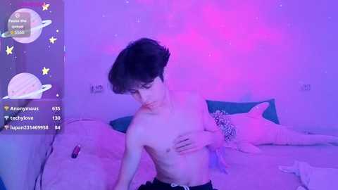 Video of a shirtless, pale-skinned young man with short dark hair, standing in a dimly-lit bedroom with a pink glow, wearing black pants.