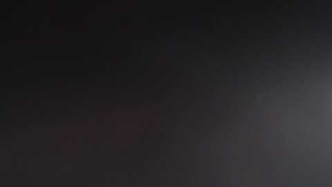 A dark, monochromatic video with indistinct, blurry figures and minimal contrast, suggesting an abstract, possibly artistic, composition. The background is predominantly black with hints of gray and faint red tones, creating an enigmatic, mysterious atmosphere.