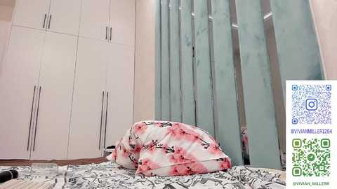 Video of a modern, minimalist bedroom with white wardrobes, a bed with a pink and white floral duvet, and a green QR code in the bottom right corner.