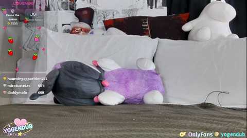 A video of a cozy living room with a plush, purple bunny and a gray bunny on a white couch, surrounded by plush toys.