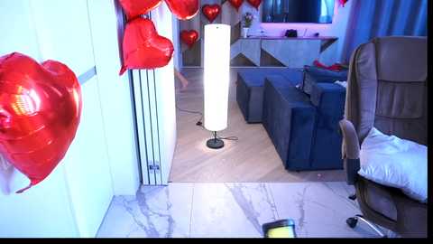 Video of a modern living room with heart-shaped red balloons, a tall white floor lamp, and a beige armchair.