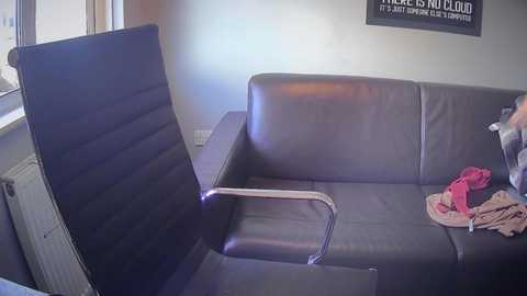 A video of a modern living room with a dark gray leather couch, an open window, a radiator, and a \"HERE'S HOLLAND\" poster on the wall.