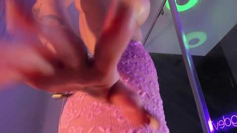 Video of a person in a purple, textured dress, wearing a large, glowing, neon green bracelet, with hands raised in a dynamic pose, against a dark background.