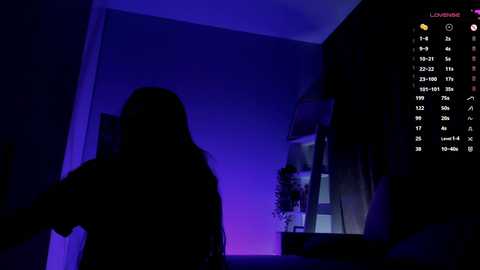 Video of a dimly lit bedroom with purple lighting, showing the silhouette of a person sitting on a bed, with a TV screen displaying a game interface.